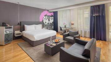 A modern hotel room with a large bed, a desk, a chair, and a sofa.