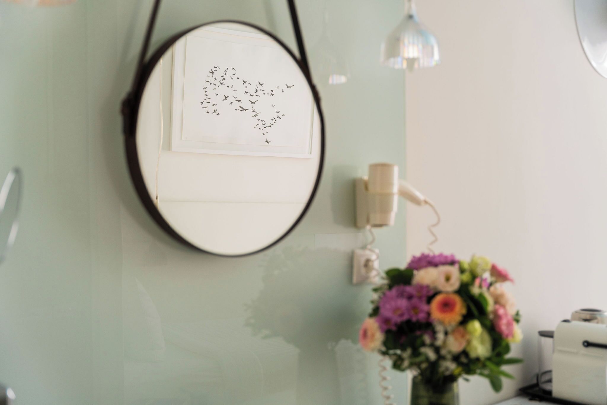 A room with a round mirror on the wall, a floral arrangement on a table, and a wall-mounted telephone.