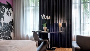 Une chambre d’hôtel avec un lit, un bureau et une chaise, une orchidée en pot et une lampe.
