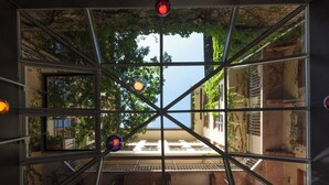 Une vue à travers une structure de fenêtre géométrique composée de plusieurs vitres, dévoilant une cour extérieure avec un escalier et de la verdure.