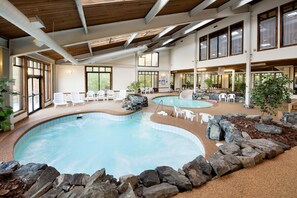 Una piscina interior con varias pistas de natación, rodeada de sillones blancos y un borde revestido de rocas.
