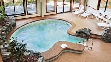 An indoor swimming pool with lounge chairs, a no children sign, and a view of the outside deck.