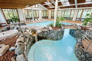 Una piscina interior con hidromasaje, rodeada de paredes de piedra y plantas, y grandes ventanales que ofrecen vistas al exterior.