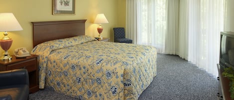 A hotel room with a large bed, two bedside lamps, a framed picture on the wall, a television, and a chair.