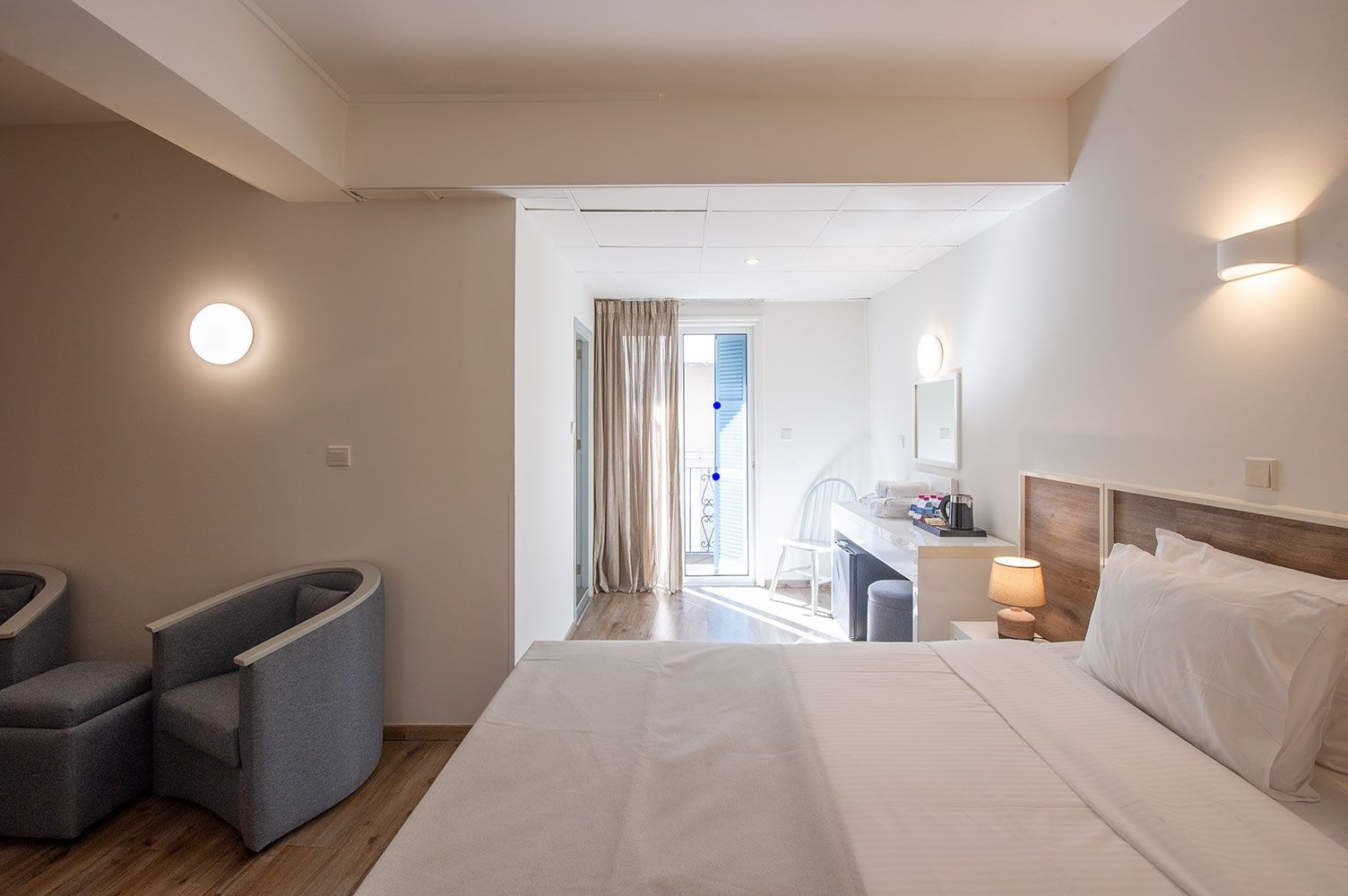 Habitación de hotel con cama, mesita de noche, lámpara y vistas al balcón.