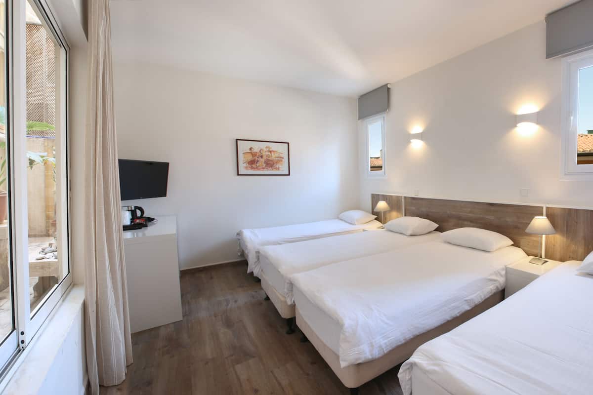 A hotel room with three beds, a TV, a desk, and a window with a view of the outside.