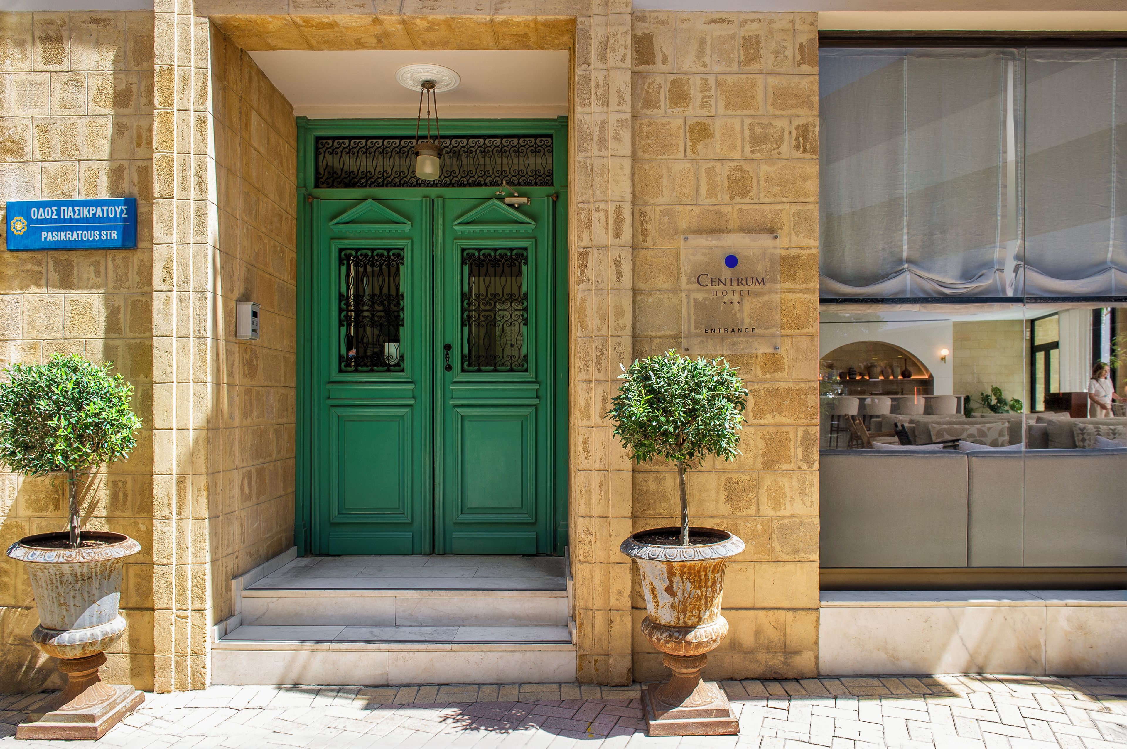 A hotel entrance with a green double door, a sign indicating the street name, and two potted plants on either side.