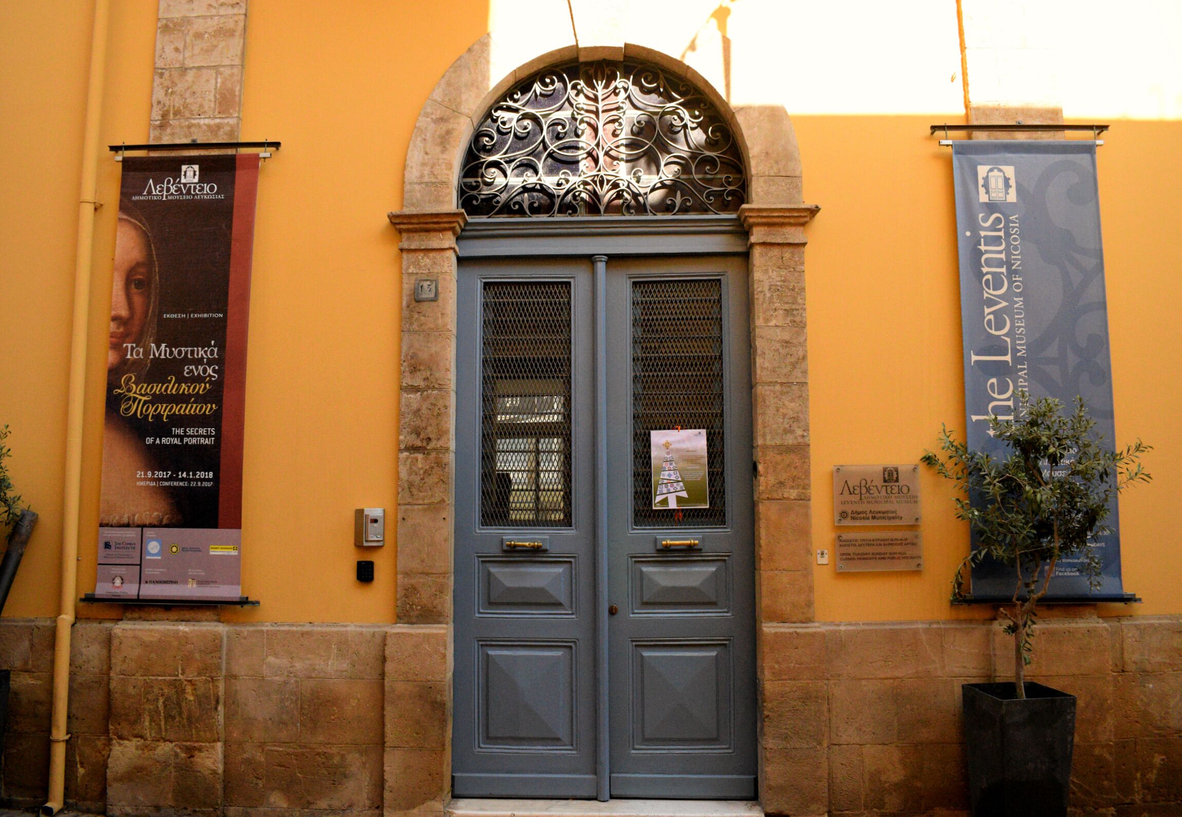 Entrada de un edificio con una puerta azul, dos pancartas y una planta en maceta.
