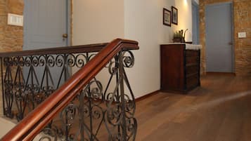 Una escalera de madera con barandillas de metal ornamentadas, un muro de piedra y una puerta azul.