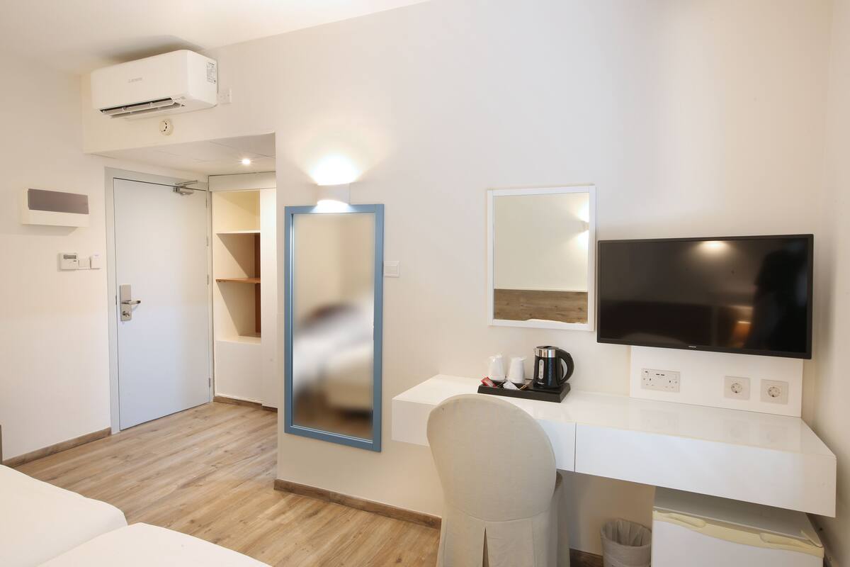 A hotel room with a bed, a desk with a computer, a TV, a mirror, and a coffee maker.