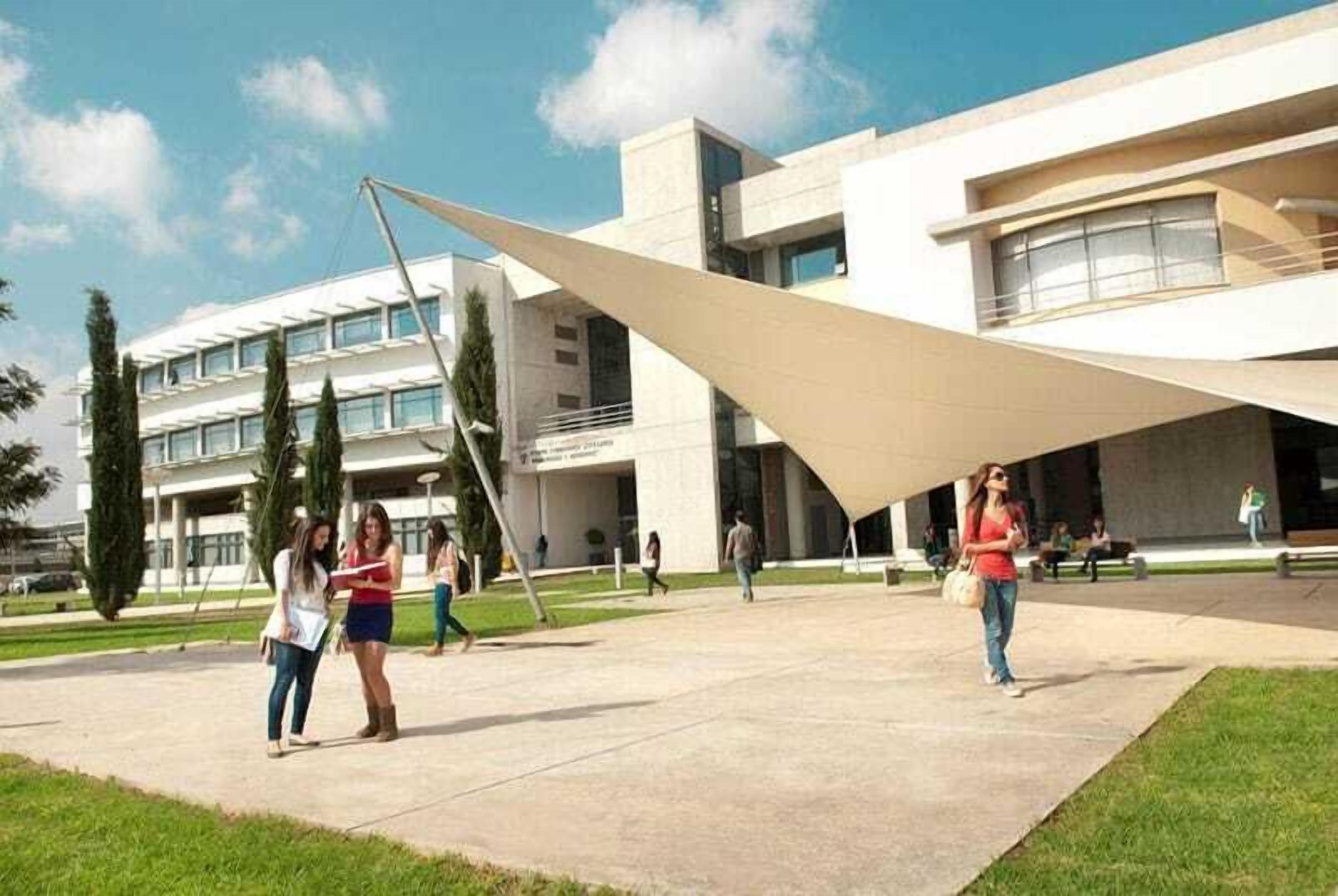 A modern building with a unique triangular roof structure and a courtyard with people walking.