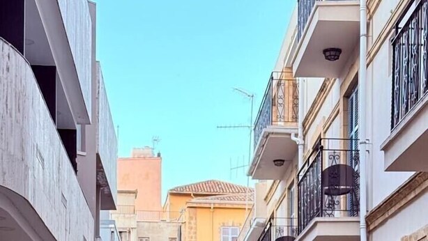 Une ruelle étroite et pavée, bordée de bâtiments dotés de balcons et de plantes en pot.