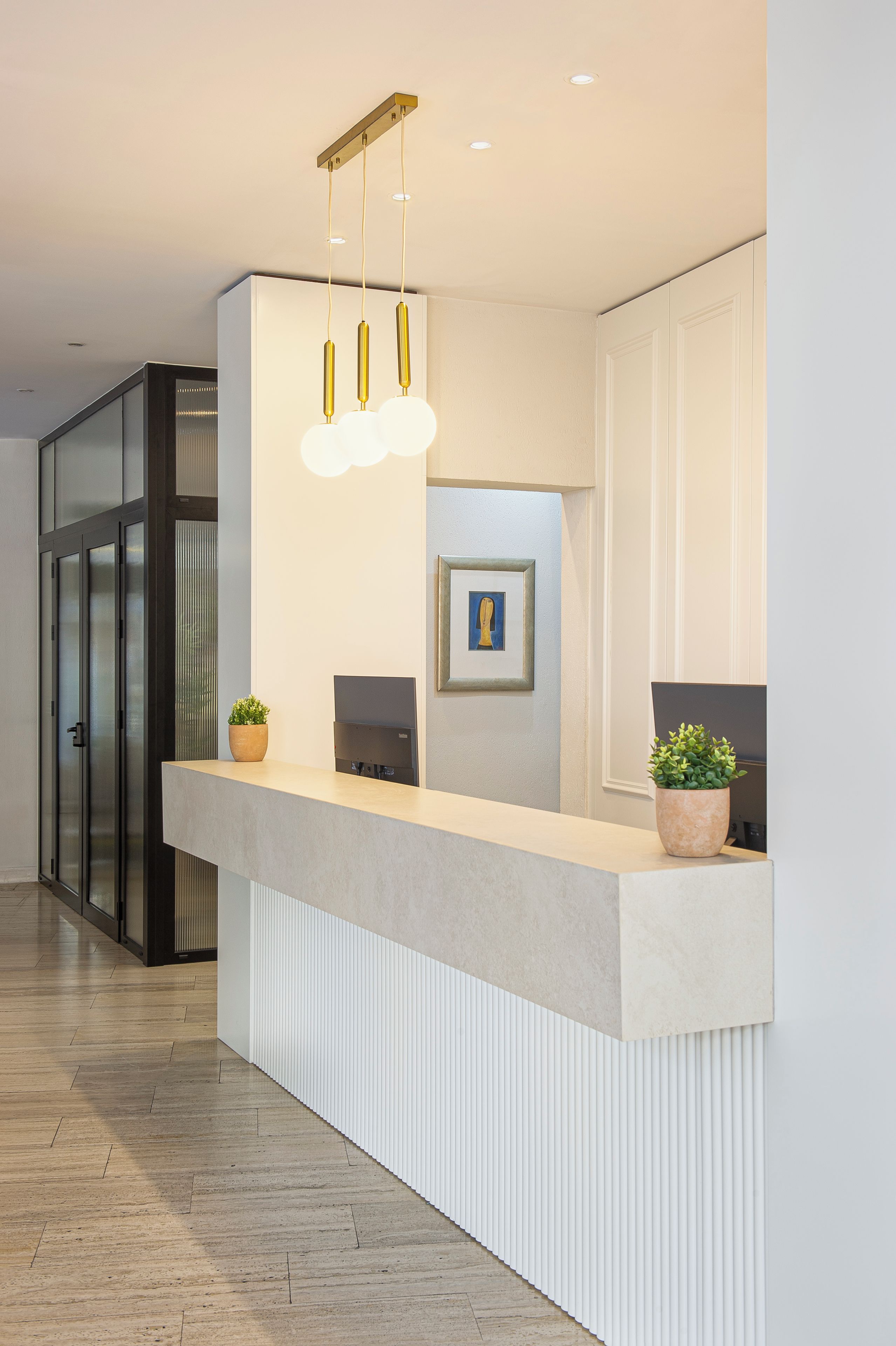 A reception desk with a modern design, a framed artwork above it, and a potted plant on the counter.