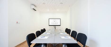 Une salle de conférence avec une longue table, des chaises noires, un écran de projection et un tableau blanc.
