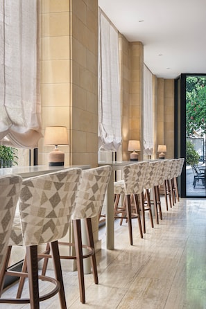 A row of bar-style seating with patterned chairs and lamps, against a wall with a geometric tile pattern. - Centrum Hotel (Nicosia)