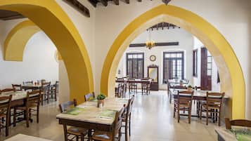 A dining area with multiple tables and chairs, wooden beams on the ceiling, and large windows.