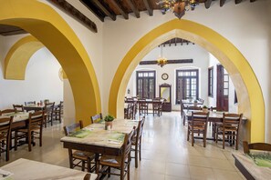 A dining area with multiple tables and chairs, wooden beams on the ceiling, and large windows. - Centrum Hotel (Nicosia)