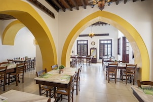A dining area with multiple tables and chairs, wooden beams on the ceiling, and large windows.