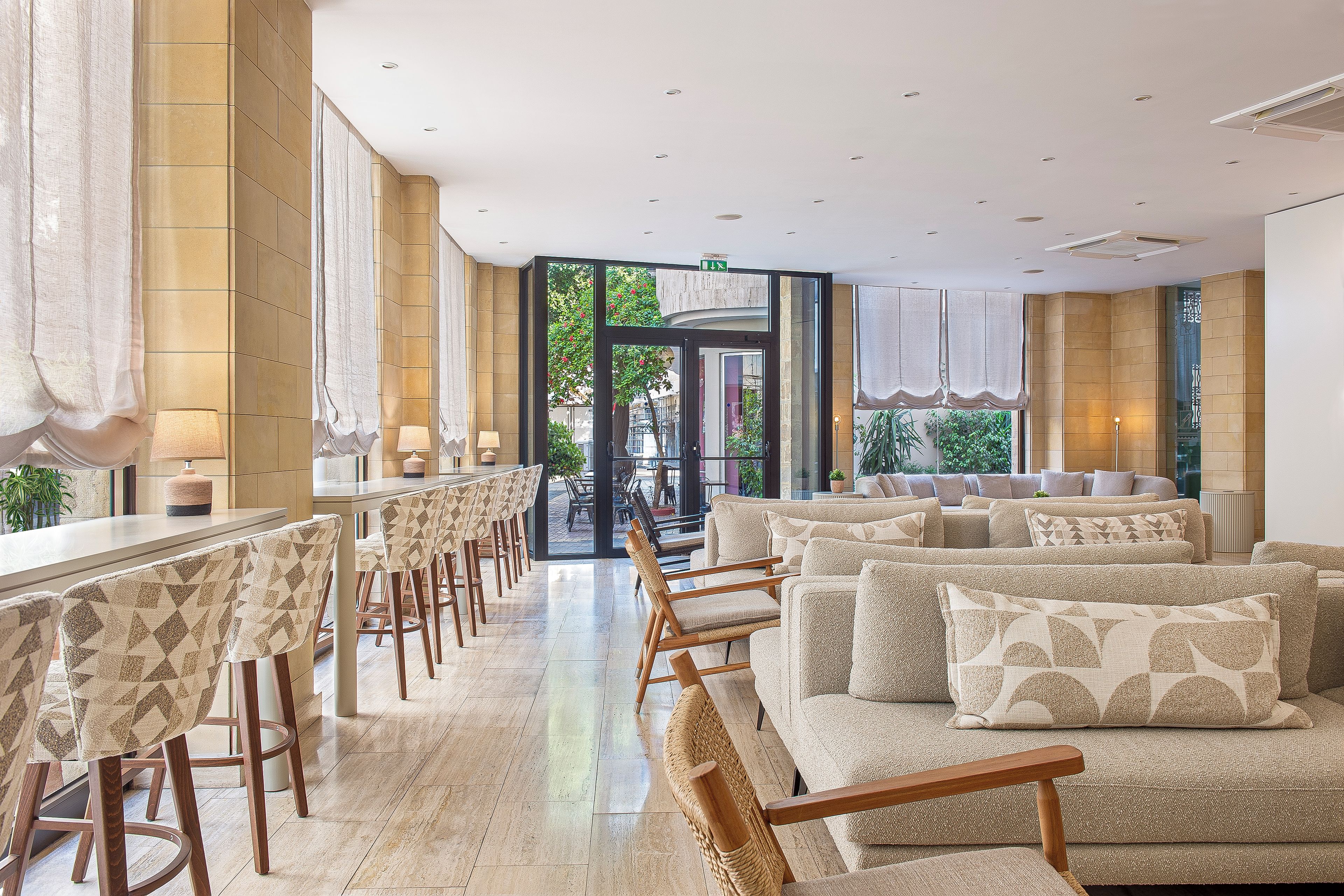 A hotel lobby with a bar area, seating, and a view through the glass doors.