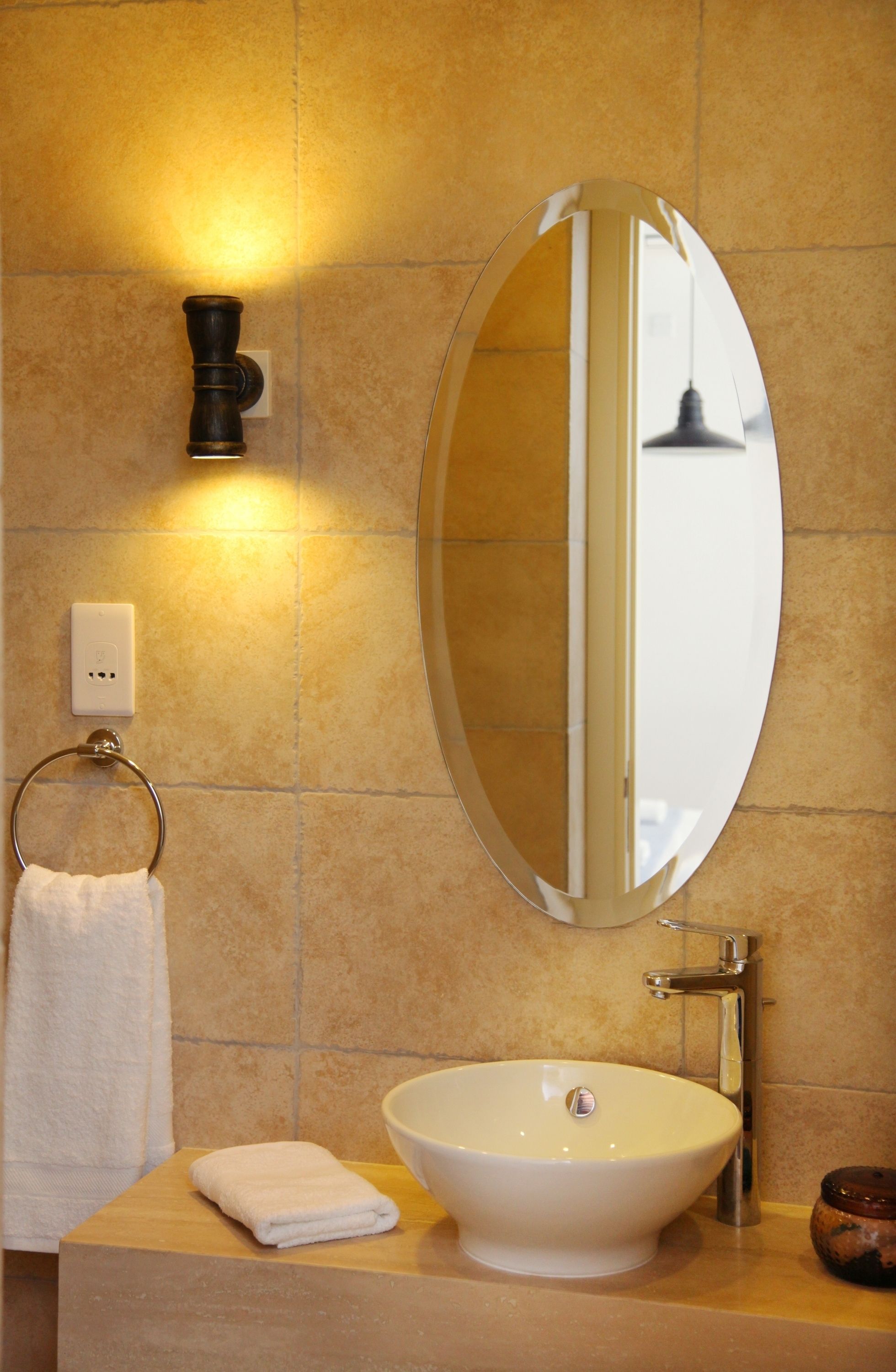 Ein Badezimmer mit rundem Spiegel, Waschbecken, Handtuchhalter und Wandleuchte.
