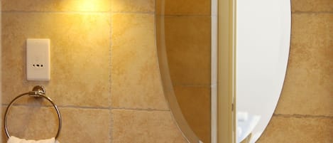 A bathroom with a round mirror, a sink, a towel ring, and a wall-mounted light.
