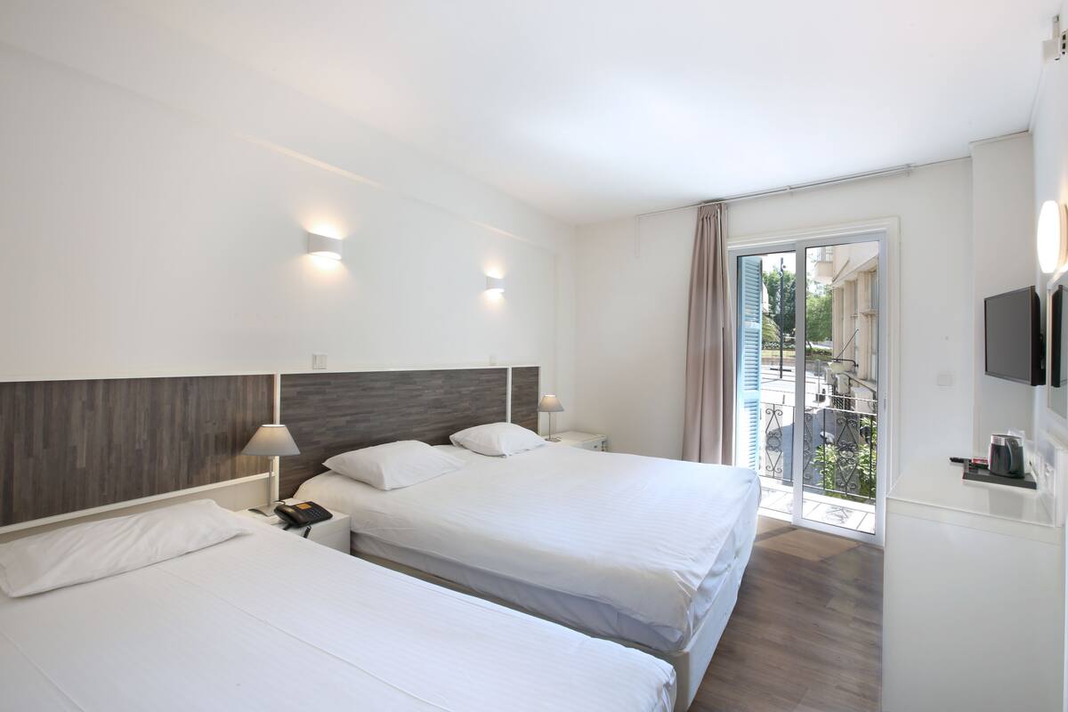 A hotel room with two beds, a balcony, a TV, and a minibar.