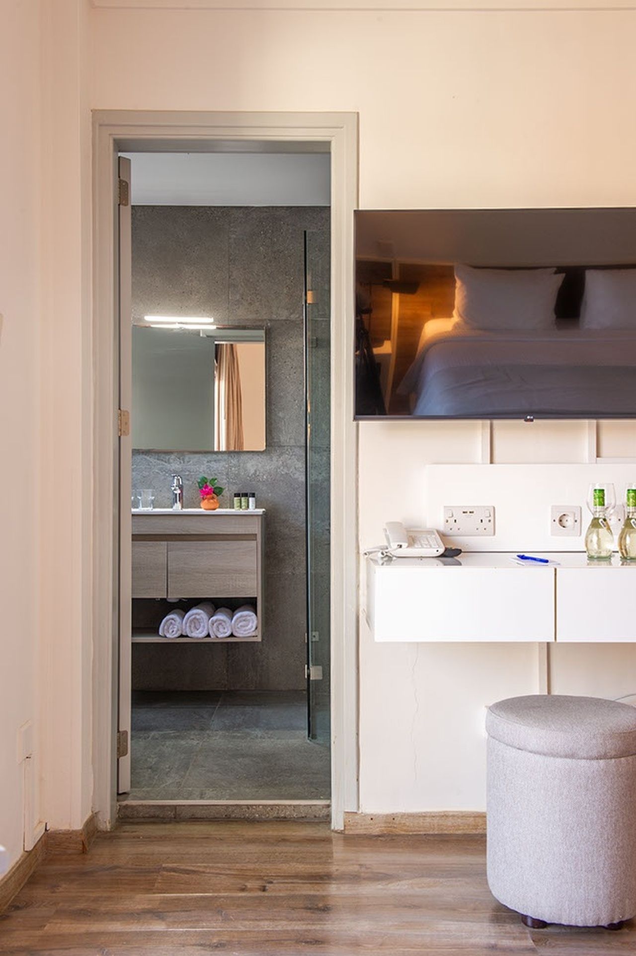 A modern bathroom with a glass door, a white vanity, and a grey ottoman.