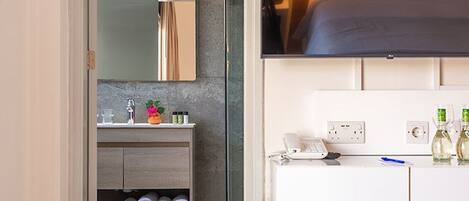A modern bathroom with a glass door, a white vanity, and a grey ottoman.