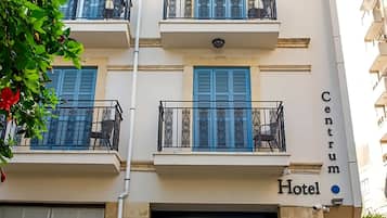 Un hotel con una entrada central, varios balcones y plantas en macetas.