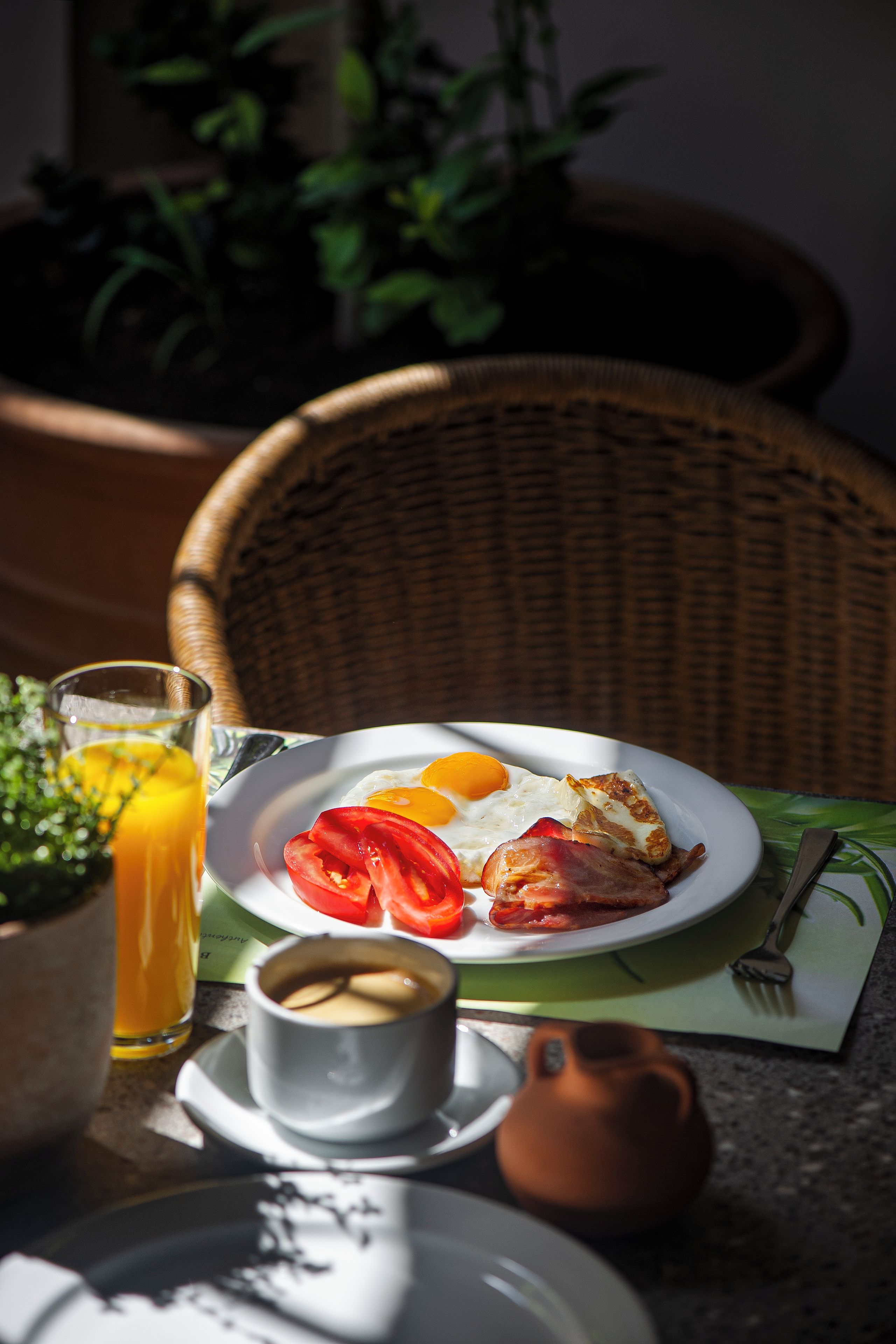 Una silla de mimbre, un plato con comida, un vaso de jugo y una taza de café.