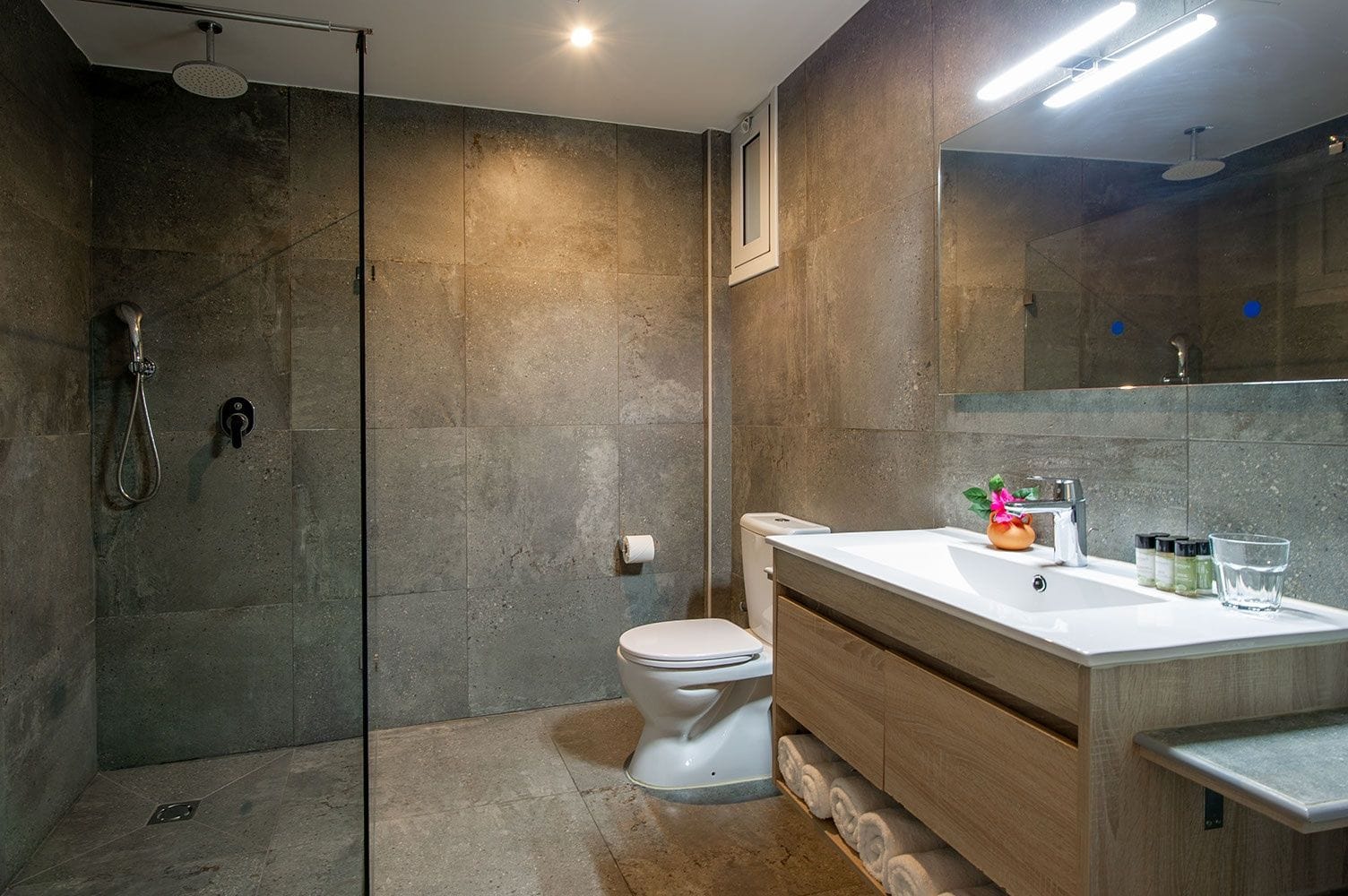 Uma casa de banho moderna com chuveiro, sanita e lavatório.