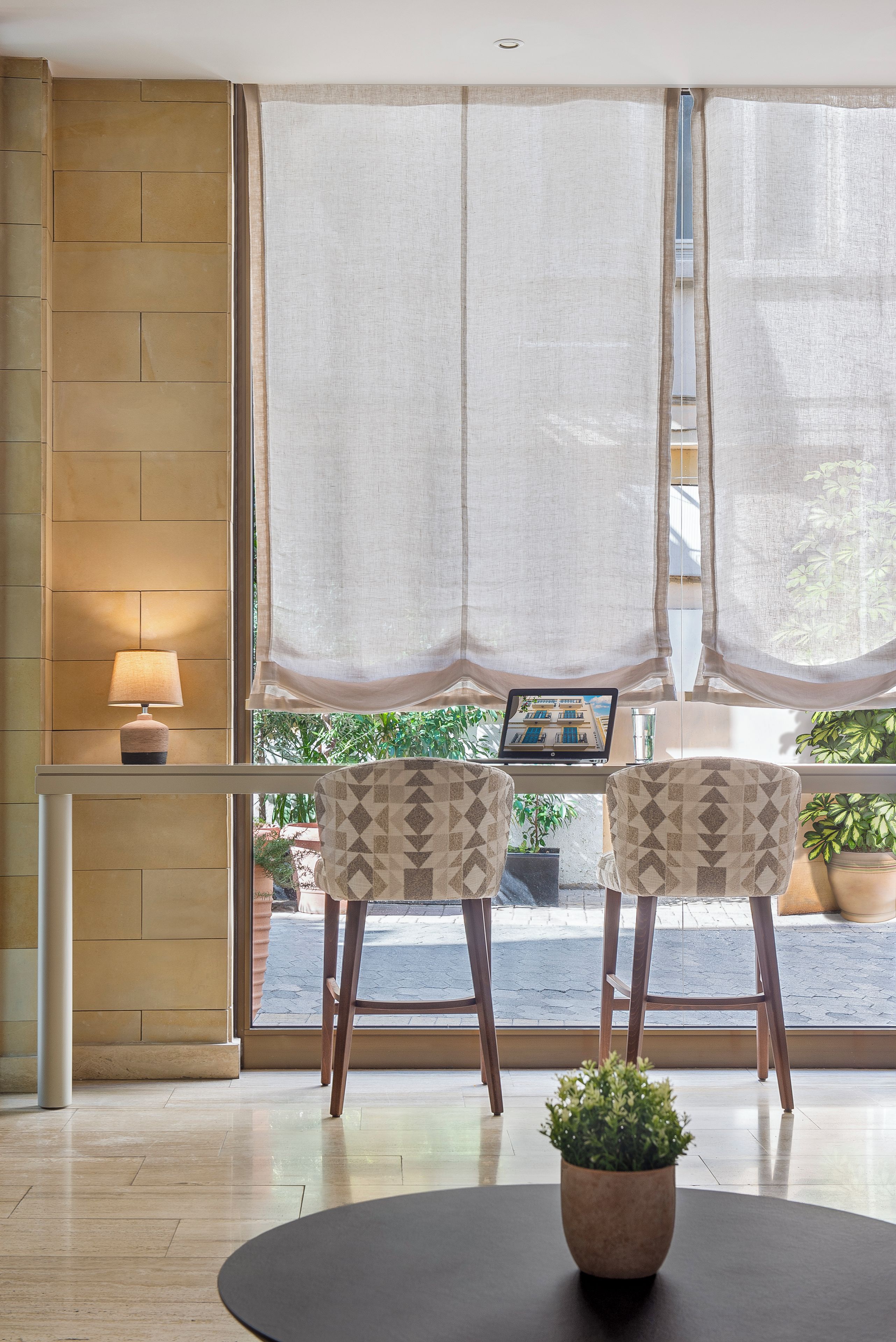A room with a large window, two chairs, a table with a potted plant, and a lamp.