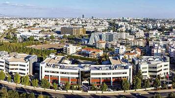 An aerial view of a cityscape with modern buildings, a highway, and surrounding greenery.