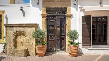A building with a stone archway, a wooden door with a metal gate, and two large terracotta planters with shrubs.