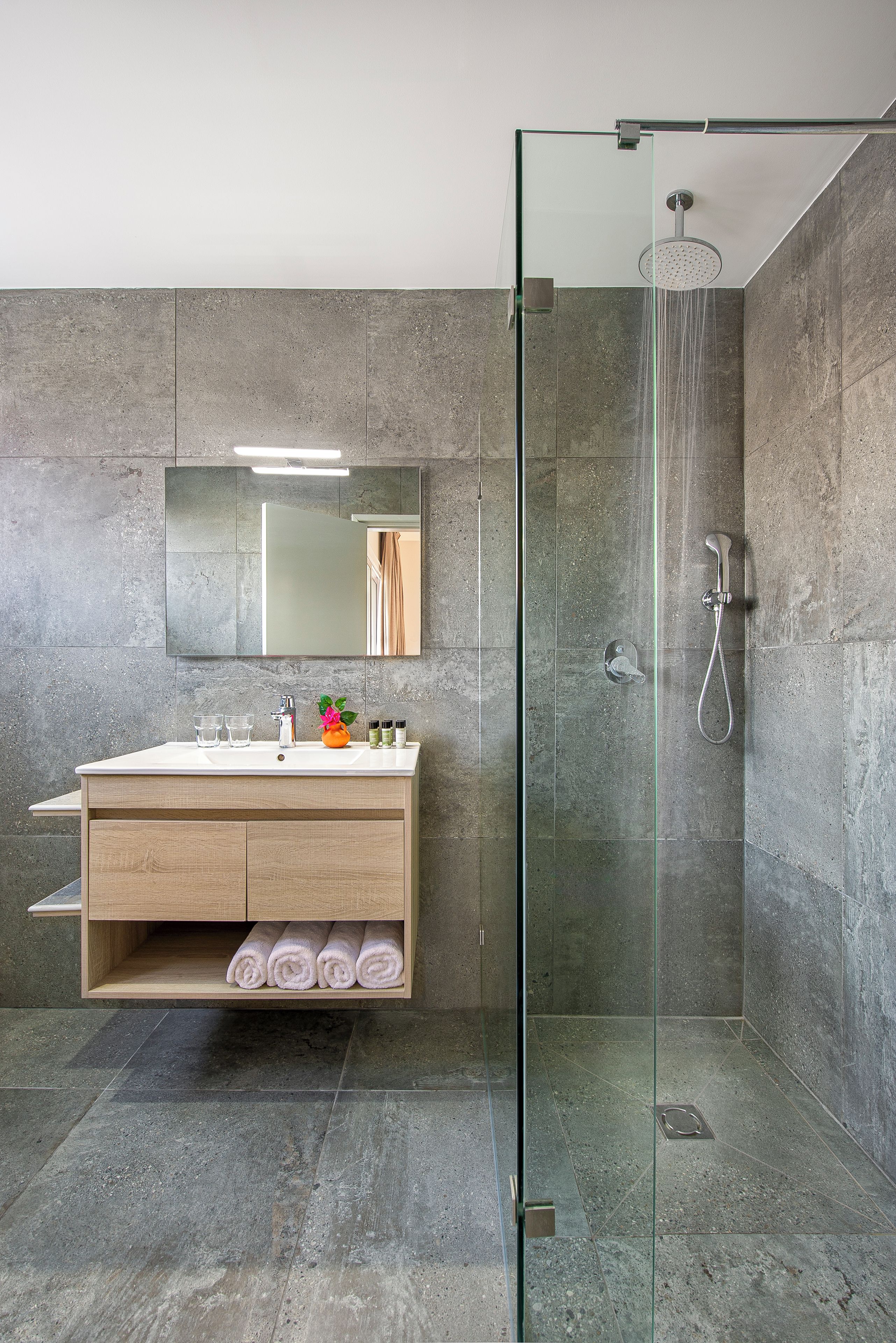 A modern bathroom with a glass-enclosed shower, a wooden vanity with a mirror, and a towel rack.
