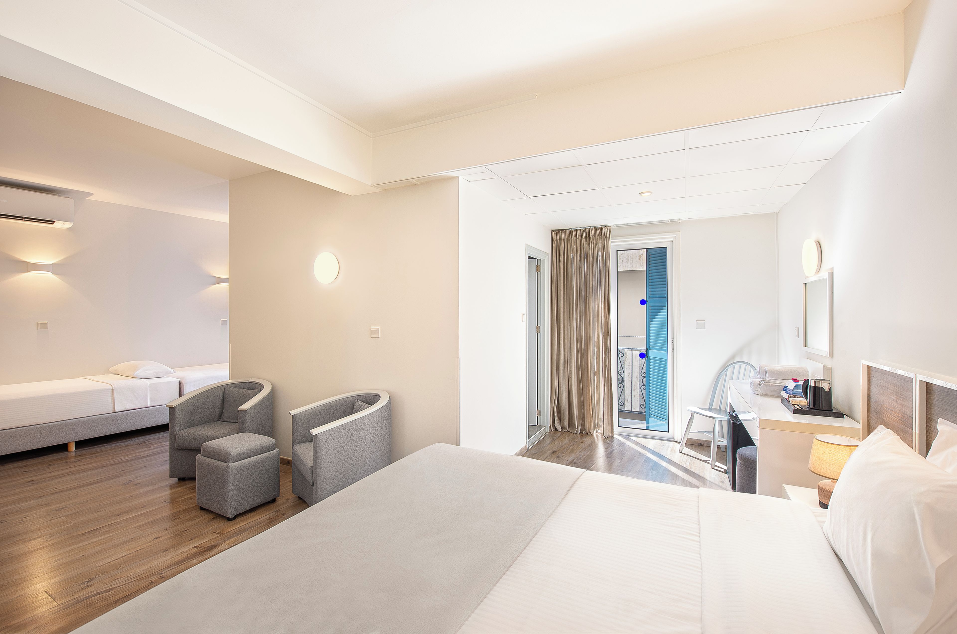 A hotel room with a large bed, two armchairs, a desk with a chair, and a view of the outside.