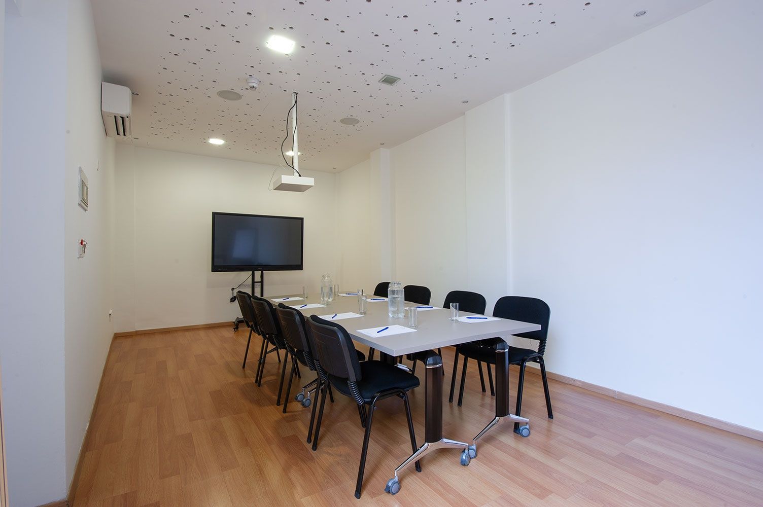 Un salón de conferencias con una gran mesa, sillas, un televisor de pantalla plana e iluminación empotrada en el techo.
