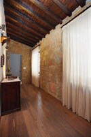 A hallway with stone walls, wooden flooring, a wooden door, and a window with curtains.