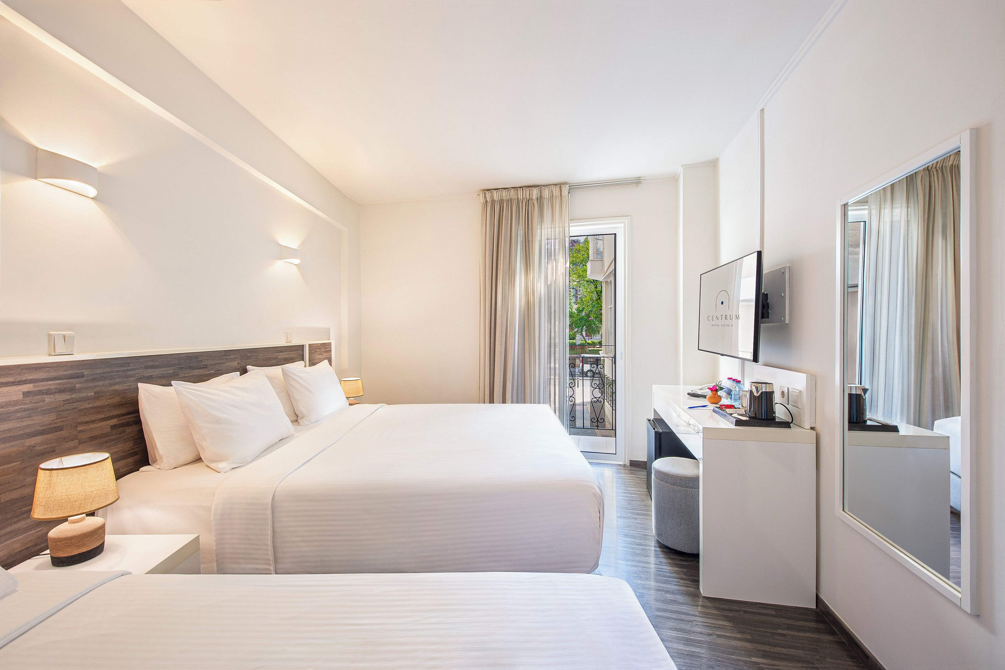 A hotel room with two beds, a desk, a TV, and a view of the outdoors.