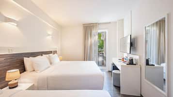 A hotel room with two beds, a desk, a TV, and a view of the outdoors.