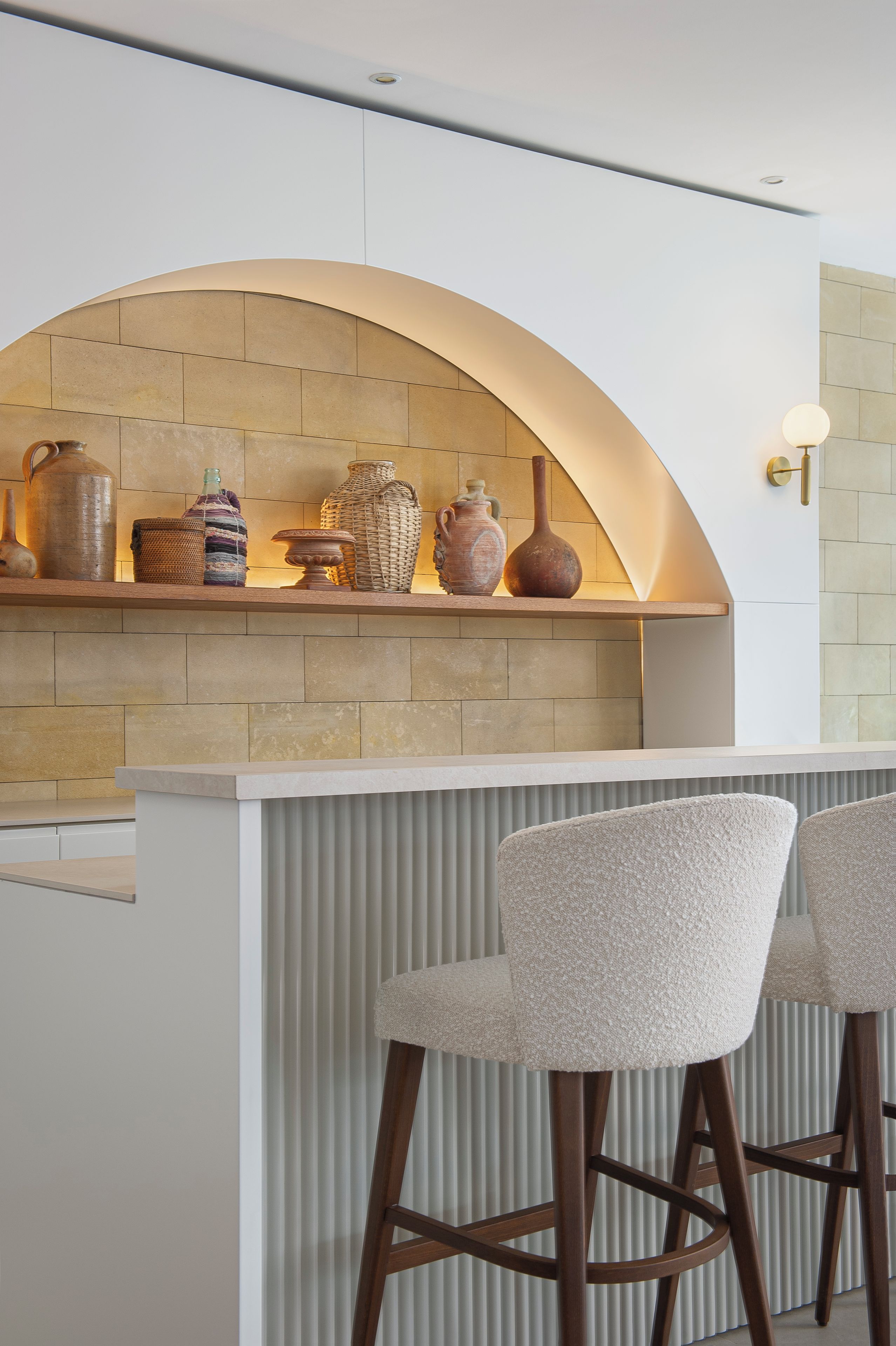 A modern kitchen with a stone backsplash, a curved arch, and a bar area with two upholstered bar stools.