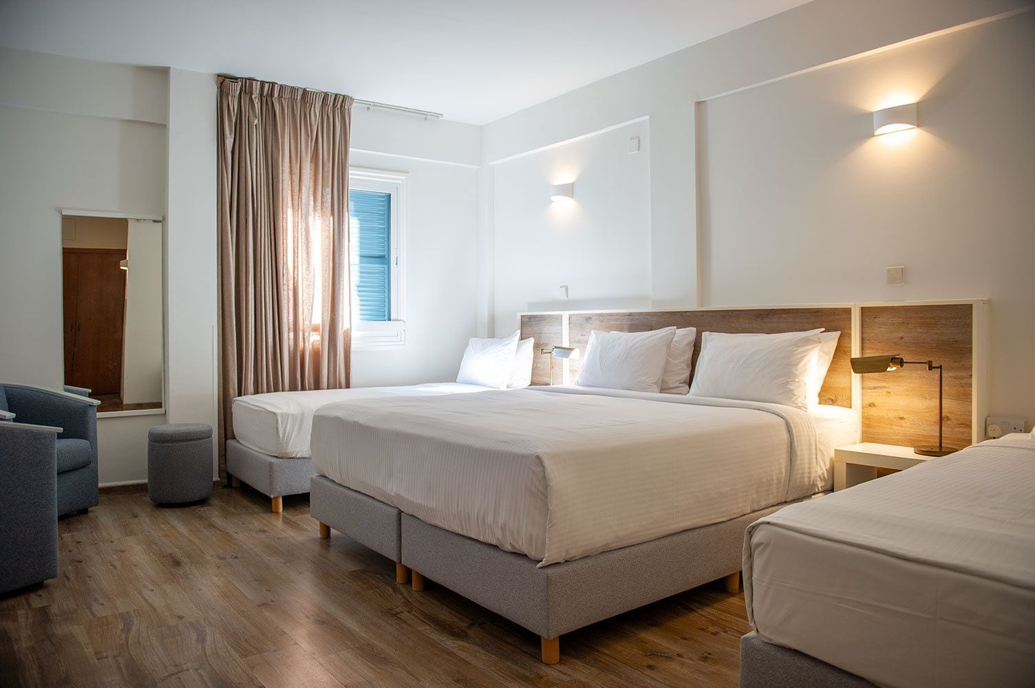 Habitación de hotel moderna con una cama grande, mesitas de noche, zona de estar y una ventana con cortinas.