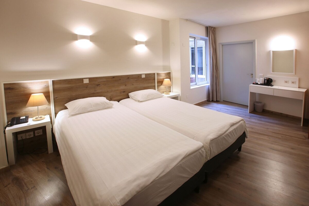 Hotellihuone, jossa on kaksi sänkyä, työpöytä, tuoli, lamppu ja ikkuna.