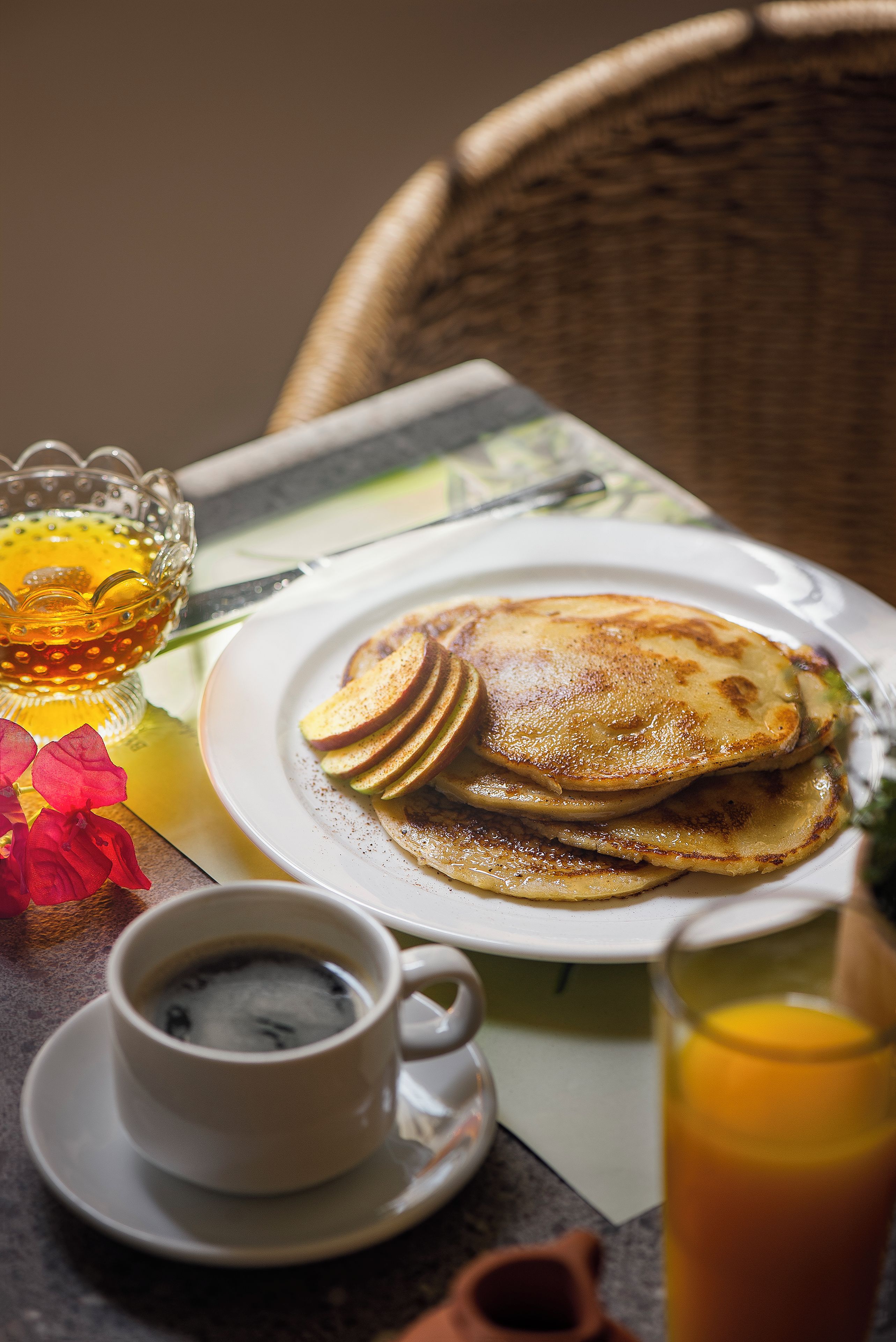 A breakfast setting with pancakes, a cup of coffee, and a glass of orange juice on a table.