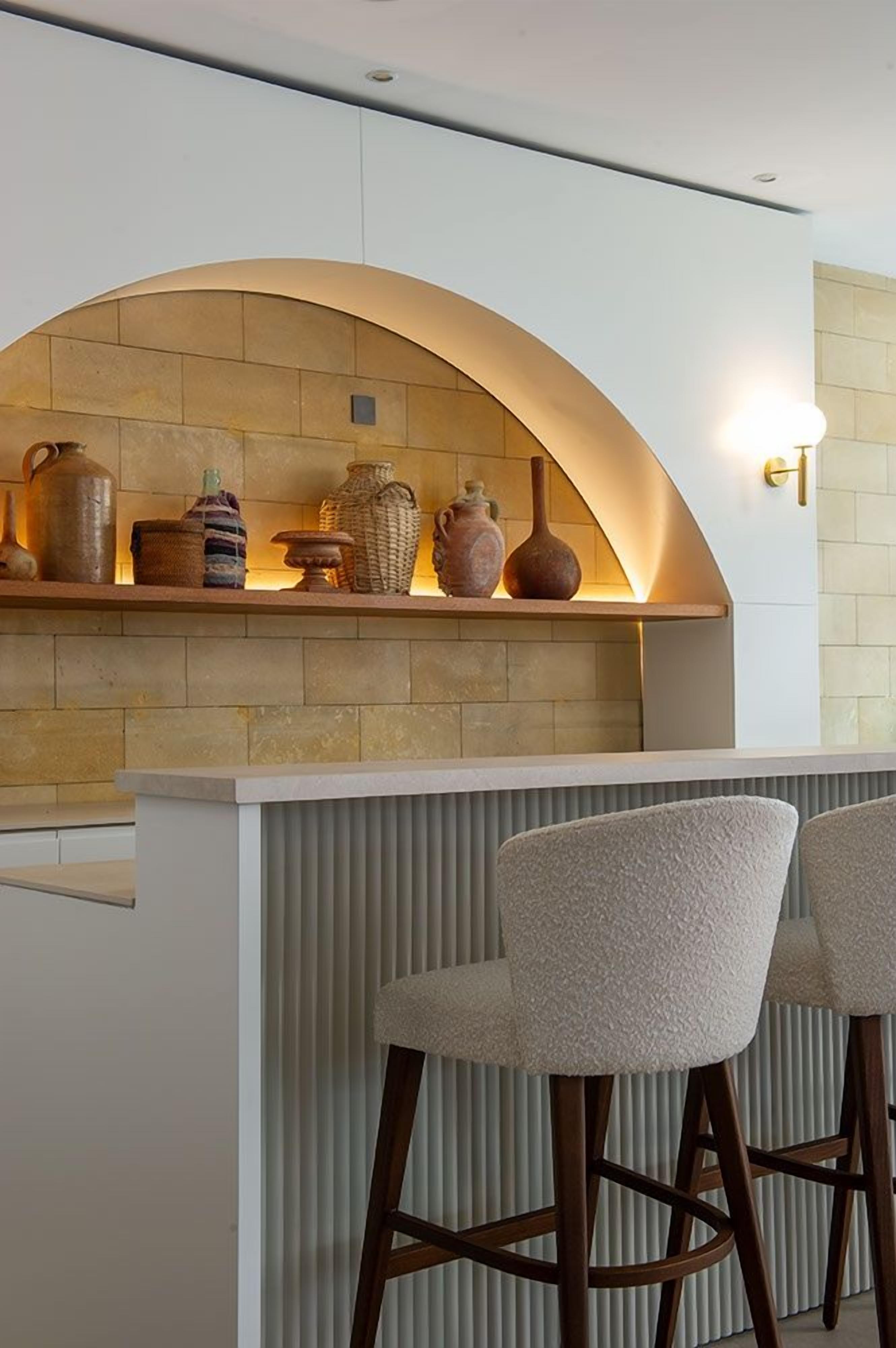 A kitchen area with a stone backsplash, a wooden bar counter, and two upholstered bar stools.