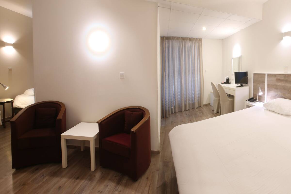 A hotel room with a large bed, a desk with a chair, a small table, and a TV.