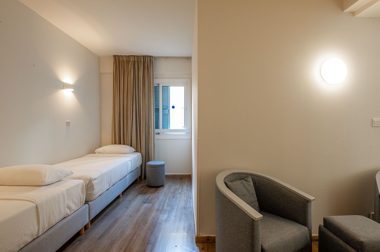 A room with a bed, a chair, a small stool, and a window with curtains.
