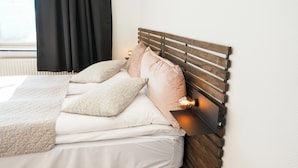 Una cama bien hecha con cabecera de madera, ropa blanca y almohadas estampadas.