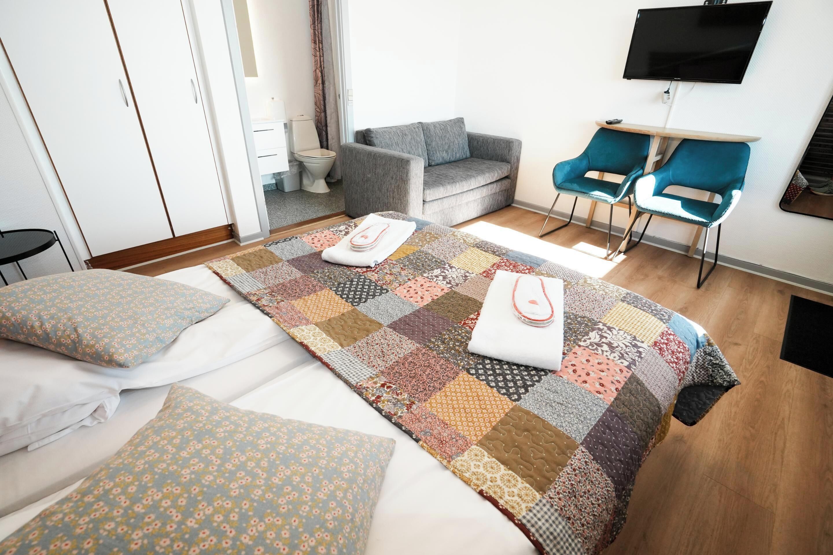 Ein Hotelzimmer mit einem großen Bett, einem grauen Sofa, zwei blauen Sesseln, einem Fernseher und einem Schreibtisch.