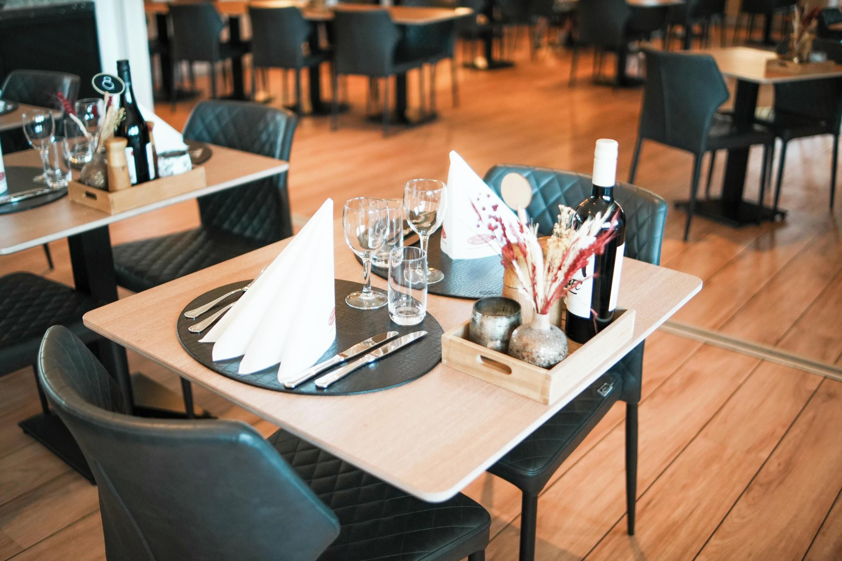 Un ambiente de restaurante con una mesa dispuesta para dos, incluyendo platos, cubiertos, copas y una botella de vino.